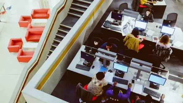 Vue en plongée d’un bureau ouvert où le personnel travaille sur des postes informatiques
