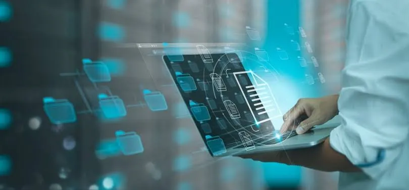 Hands holding a tablet showing digital files and folders, with a server room behind
