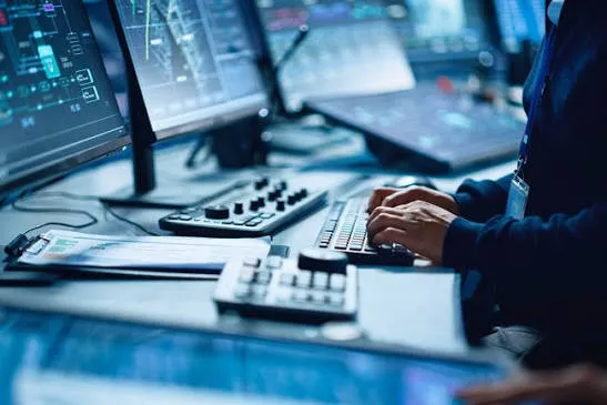 Analyst working at a multi-monitor security operations desk with data dashboards