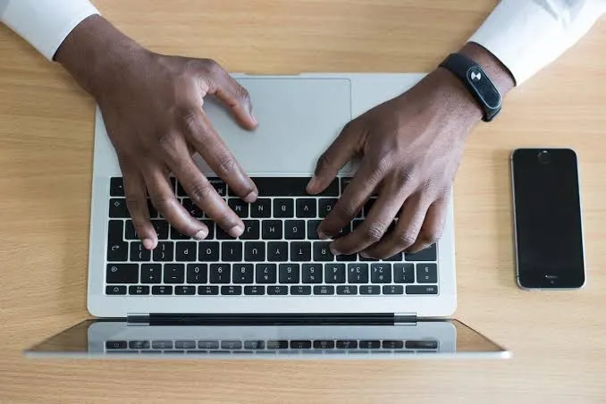 Overhead view of hands typing on a laptop keyboard next to a smartphone on a desk