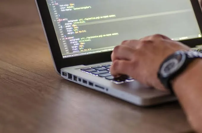 Close-up of a hand typing on a laptop with CSS code visible on screen