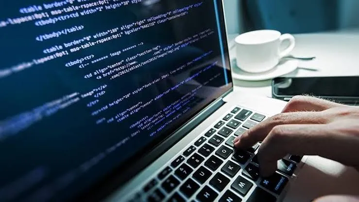 Main tapant sur le clavier d’un portable avec du code HTML affiché à l’écran